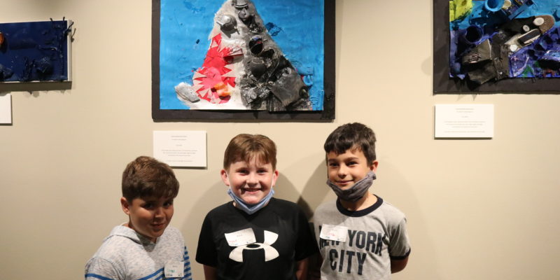 Three boys stand in front of recycled art piece