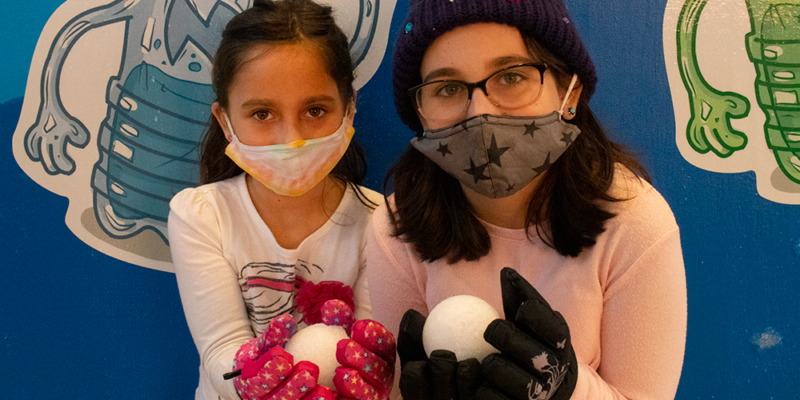 Two girls in winter gear hold a snowball