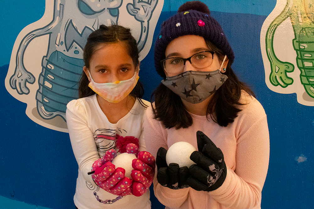 Two girls in winter gear hold a snowball