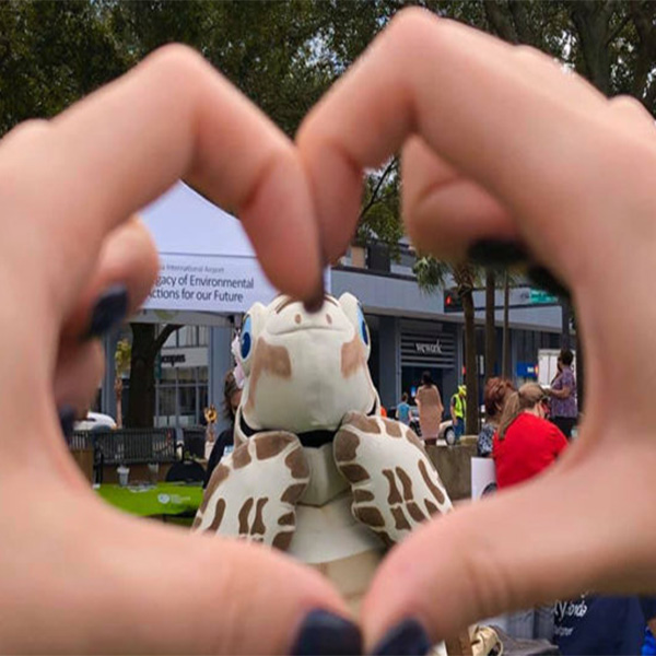 hand creating a heart around Tango the Turtle mascot