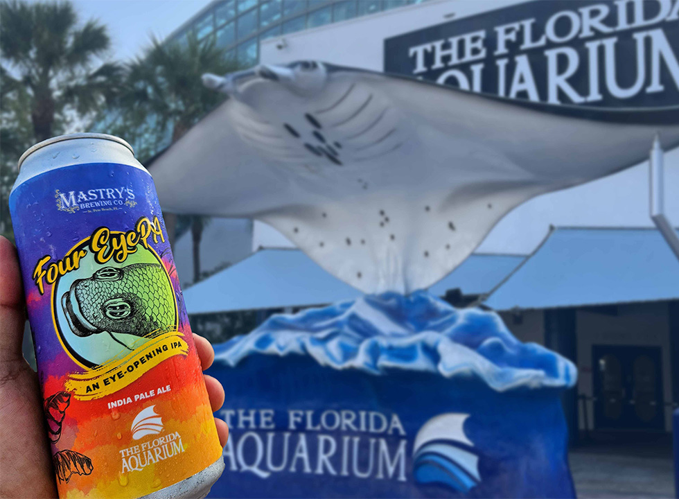 man holding a can of Mastry's Brewing Four EYEPA beer in front of a manta ray statue that says The Florida Aquarium