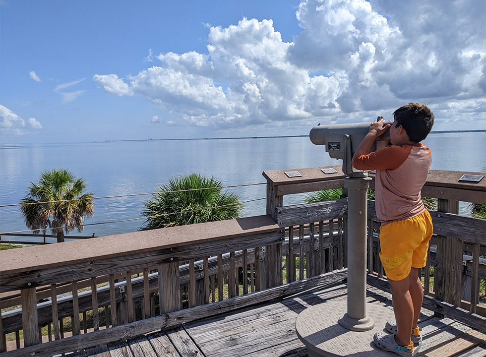 boy looking at water through tower binoculars