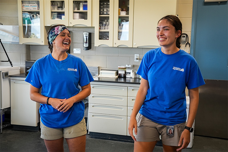 two_female_employees_laughing_in_vet_exam_room_wearing_blue_shirts_750x500