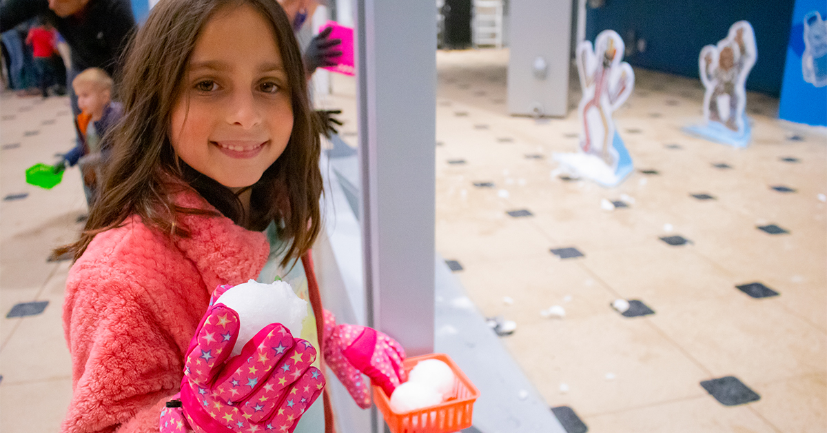 girl in pink jacket and pink gloves smiling and holding a snowball