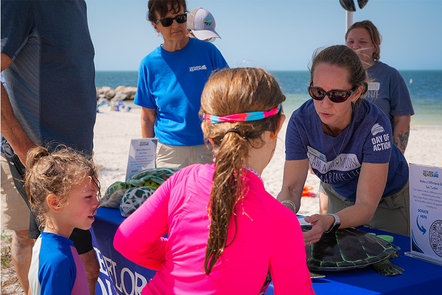 Female Aquarium employee engaging with two young girls at beach tabling event