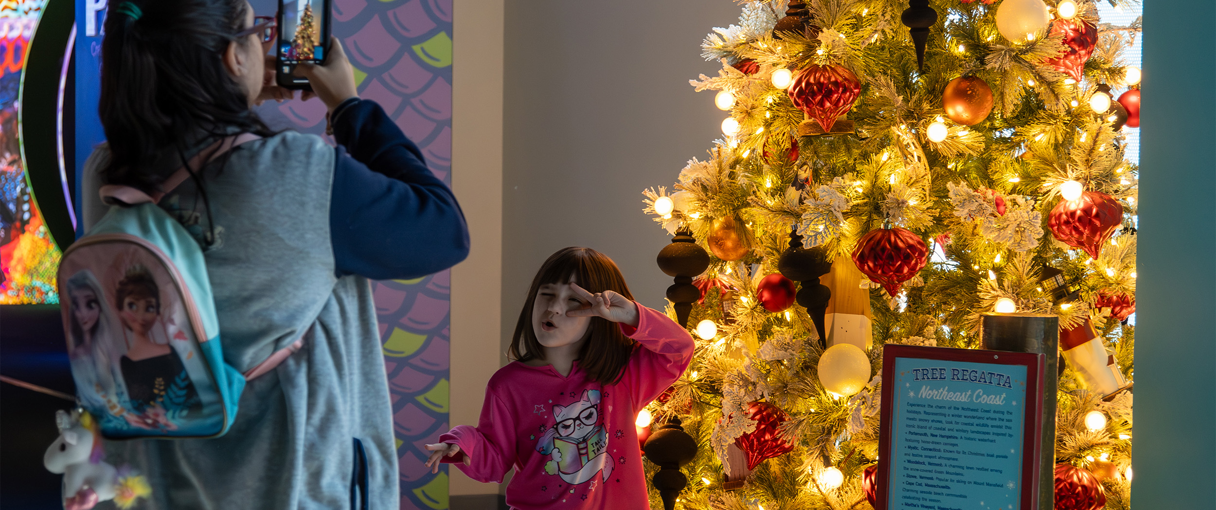 Mom taking photos of little girl in front of tree at Yuletides at The Florida Aquarium