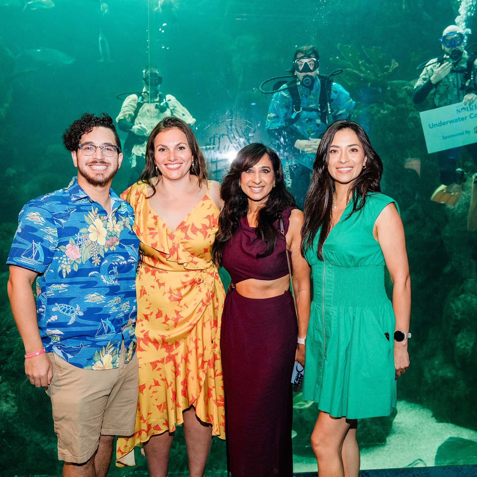 One man and three women pose in front of divers in the Shark Reef pan window at The Florida Aquarium