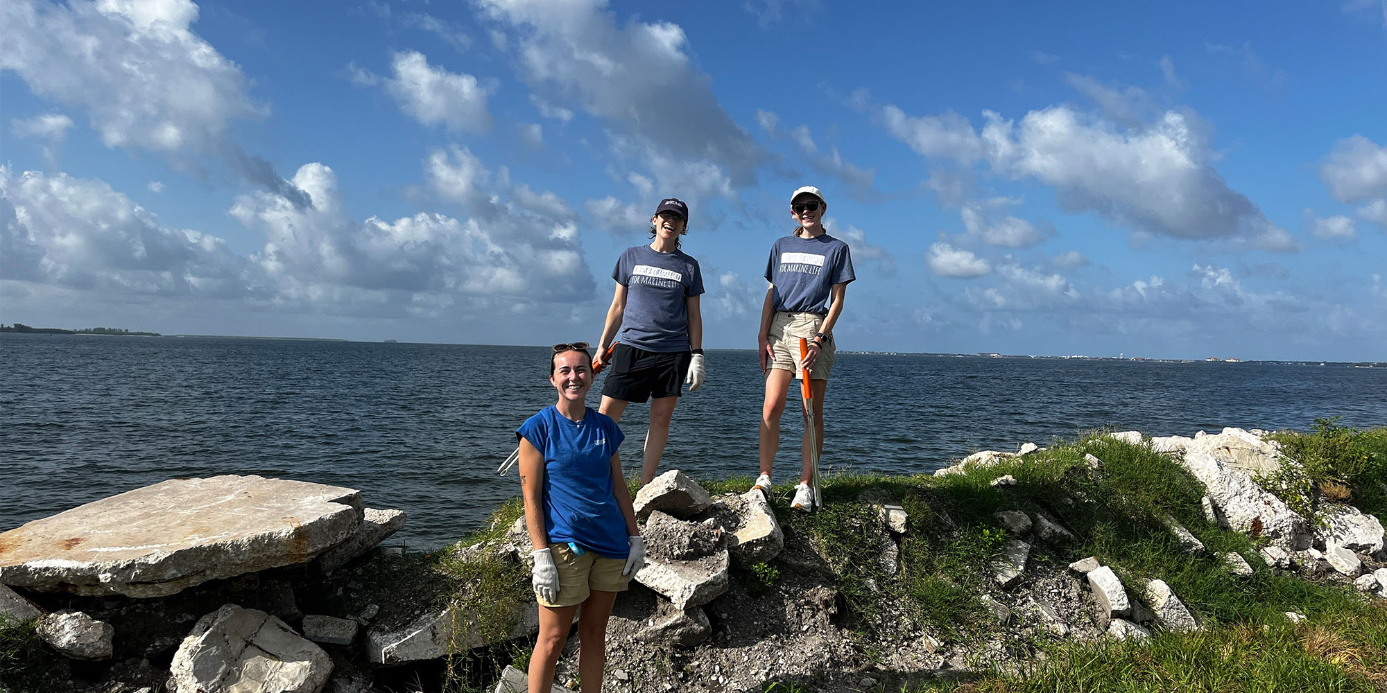 Three women standing on rocks in front of the water