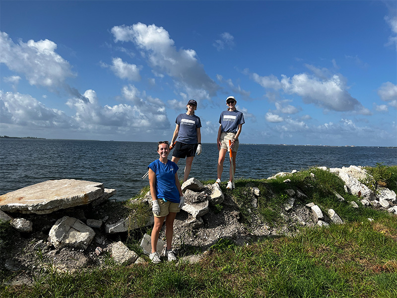 Three women standing on rocks in front of the water