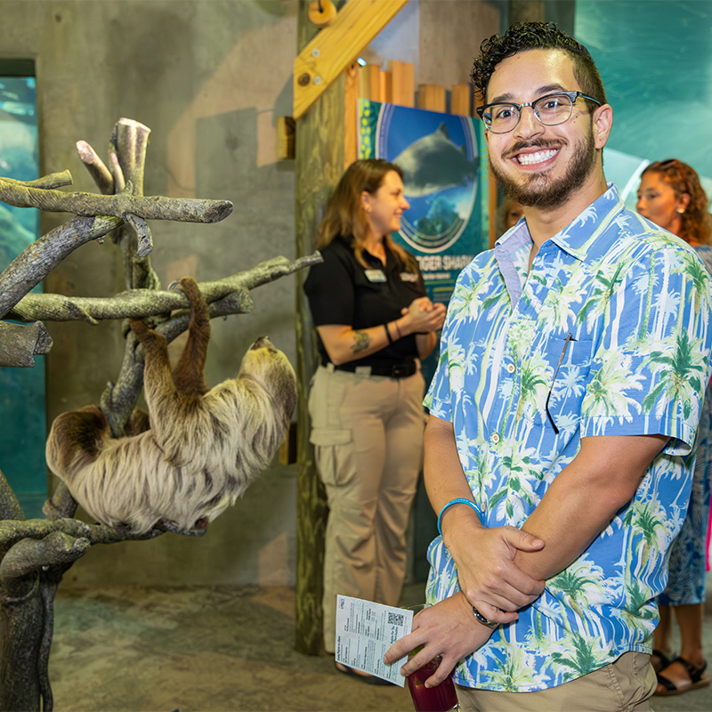 Man stands next to a sloth on its perch
