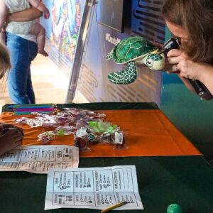 Woman checking ears of turtle stuffie while kids watch for Cuddle Clinic